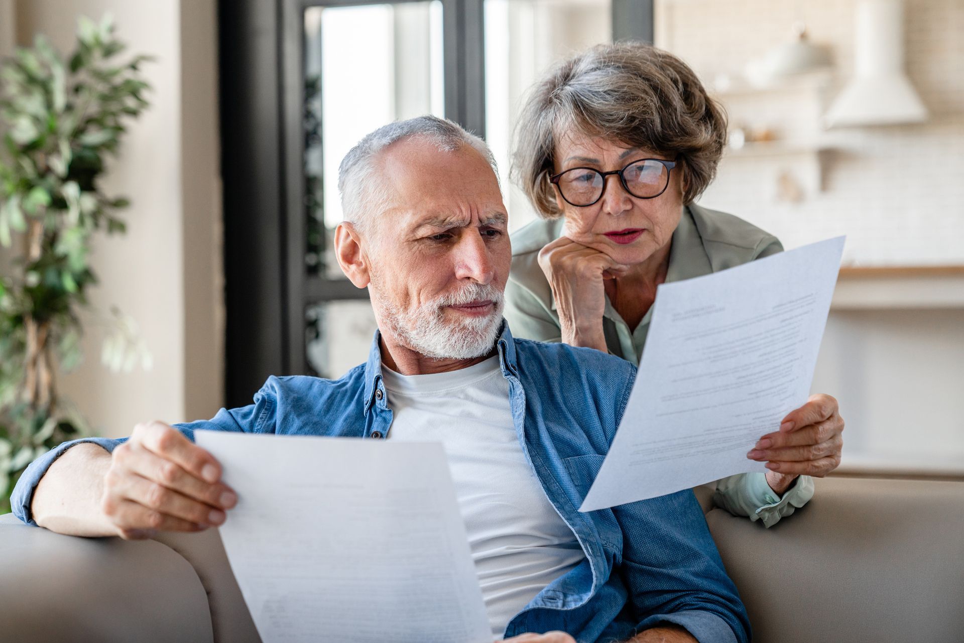 An elderly couple is sitting on a couch looking at a piece of paper.