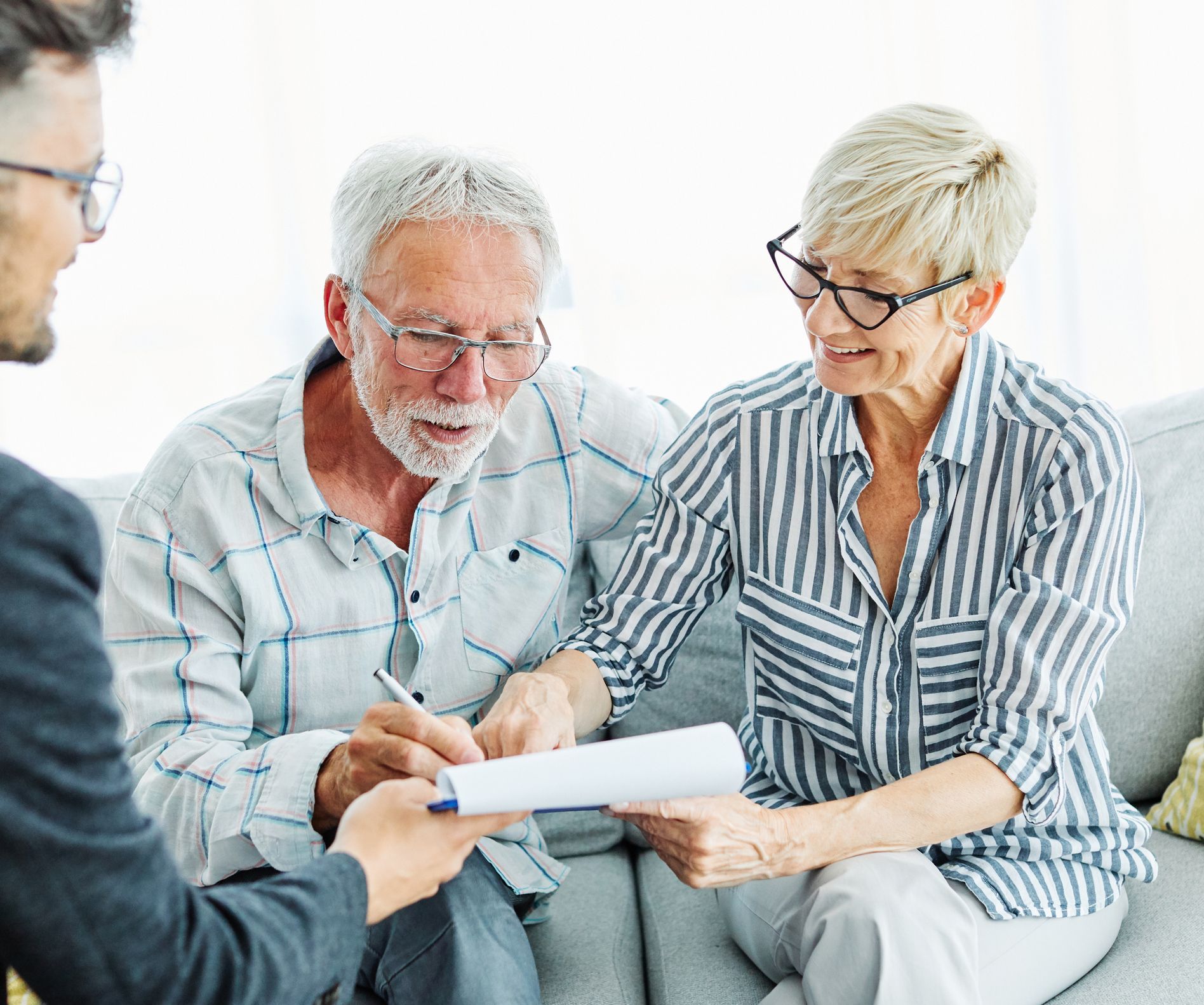 An elderly couple is sitting on a couch signing a document.