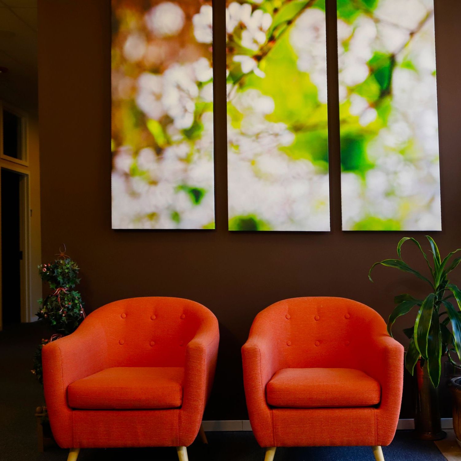 Two orange chairs in front of a wall with three paintings of flowers on it