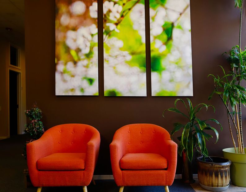 Two orange chairs are sitting in front of a wall with three paintings on it.