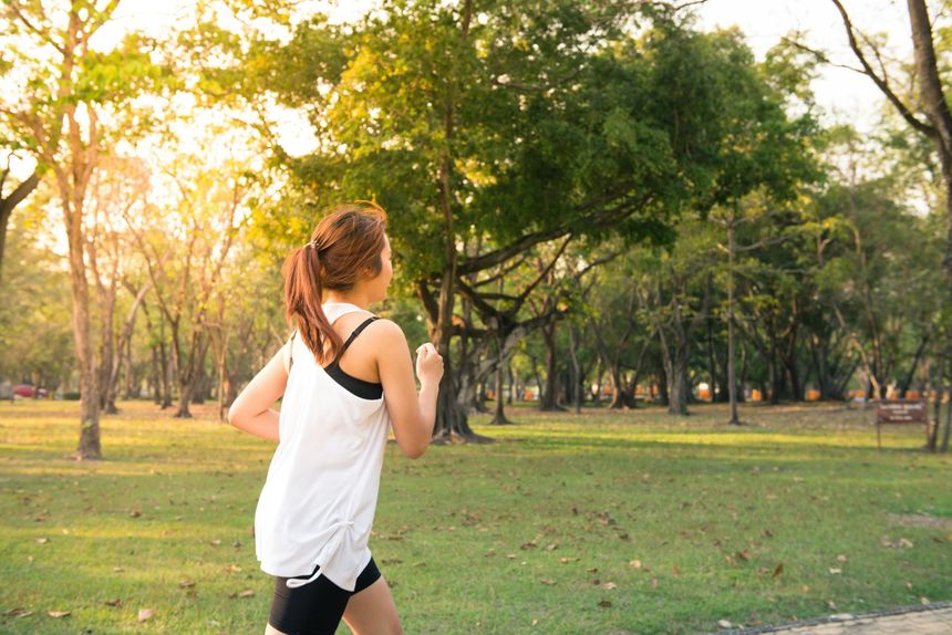 A woman is running in a park with trees in the background.
