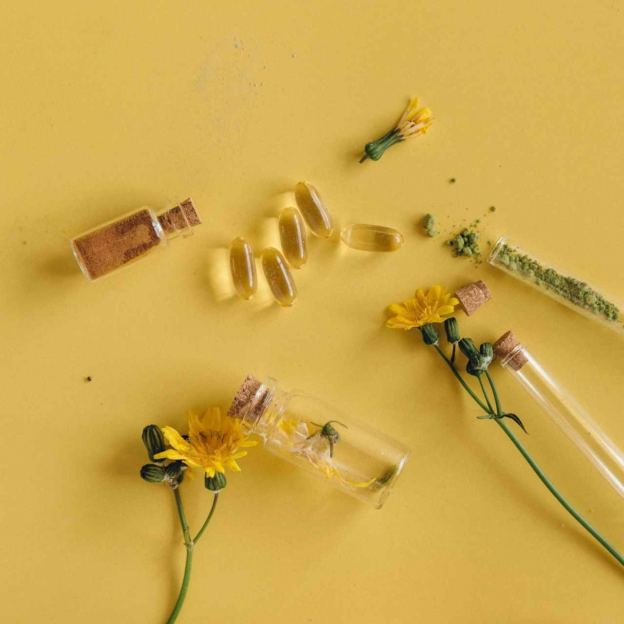 A yellow background with bottles of pills and flowers on it.
