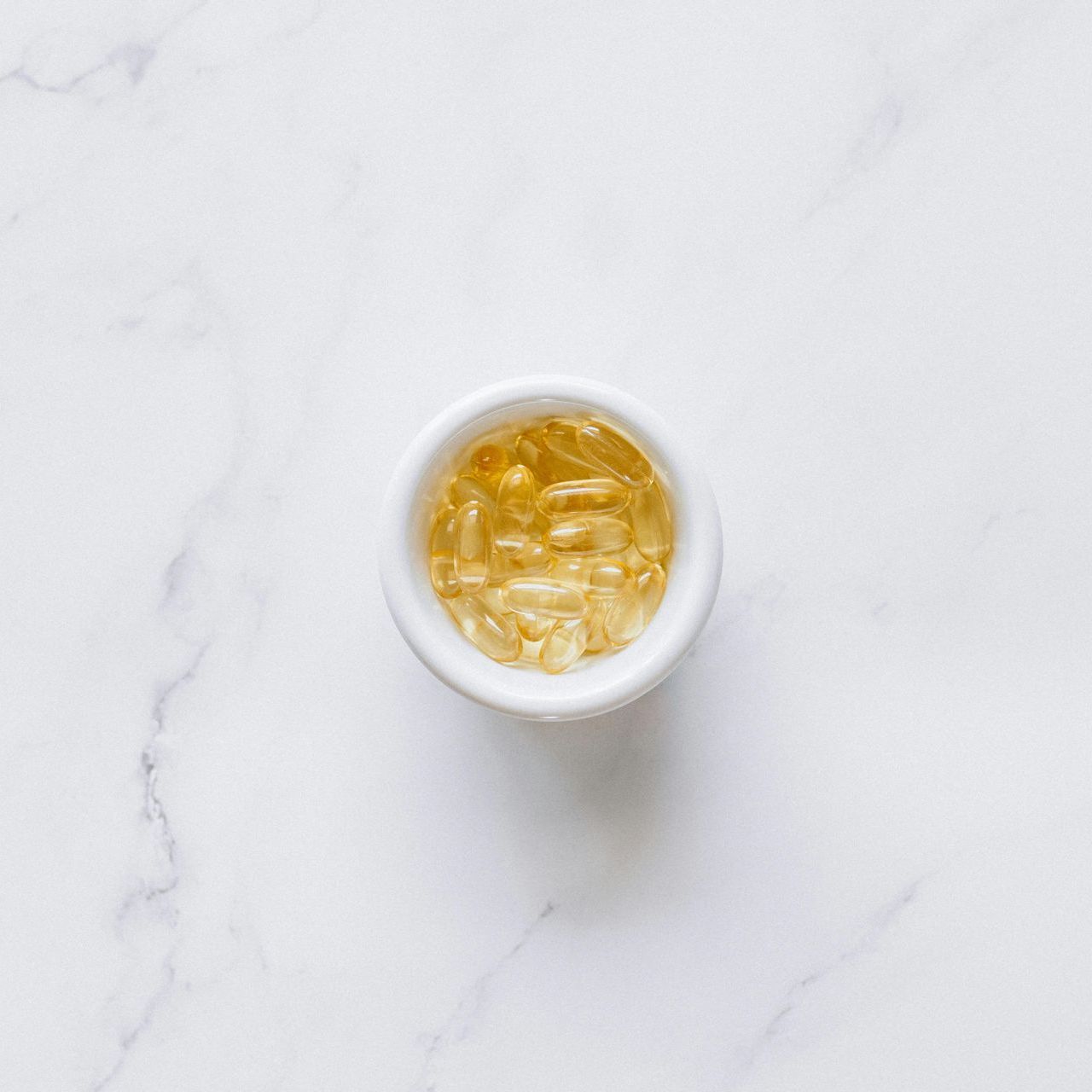 A white bowl filled with fish oil capsules on a white surface.