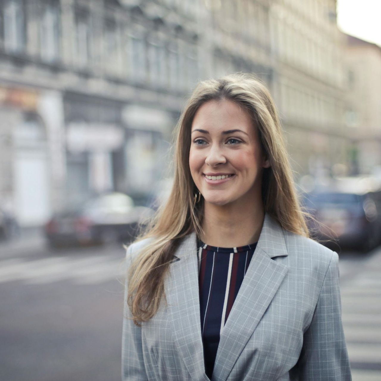 A woman in a suit is smiling while standing on a city street.