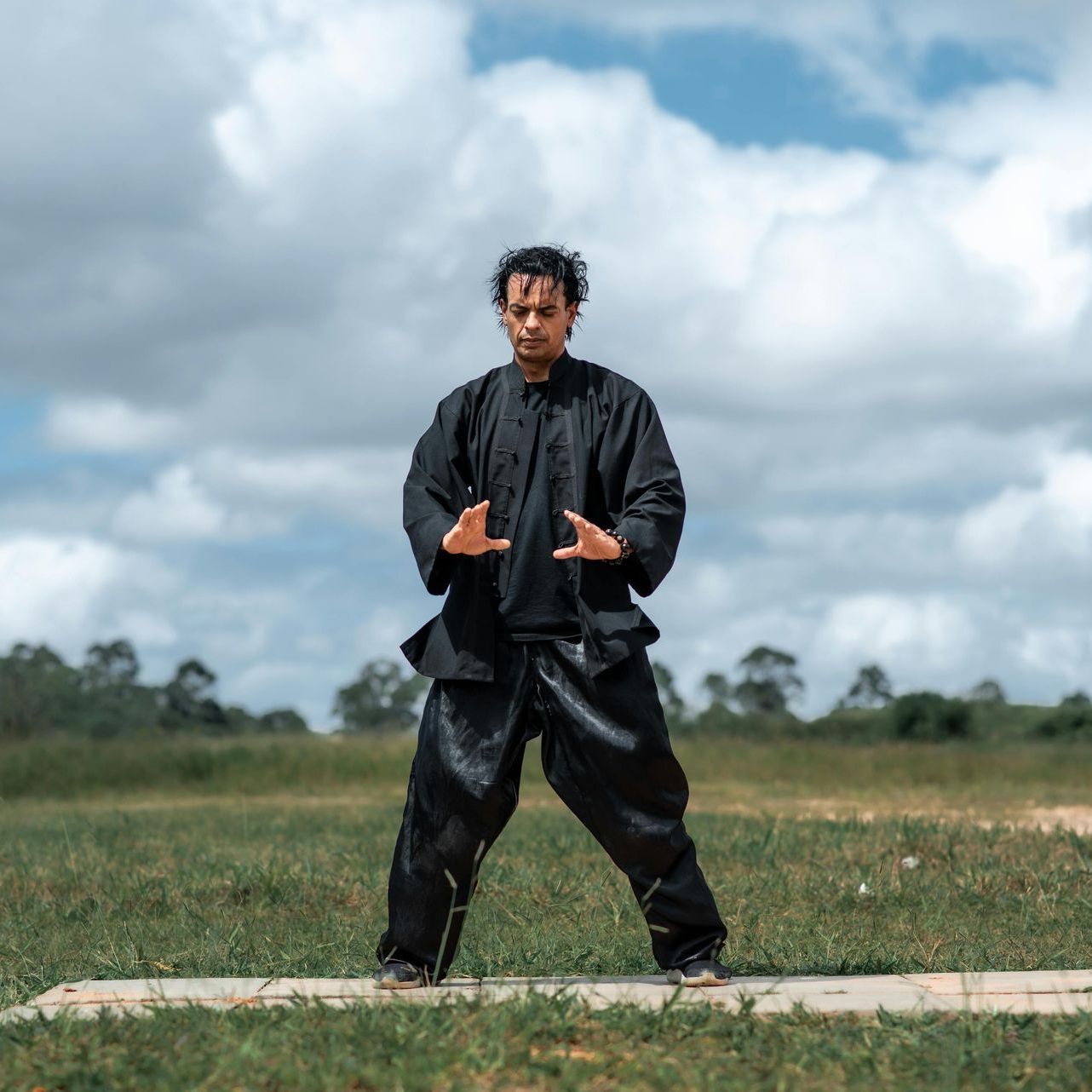 A man in a black jacket and black pants is standing in a field.