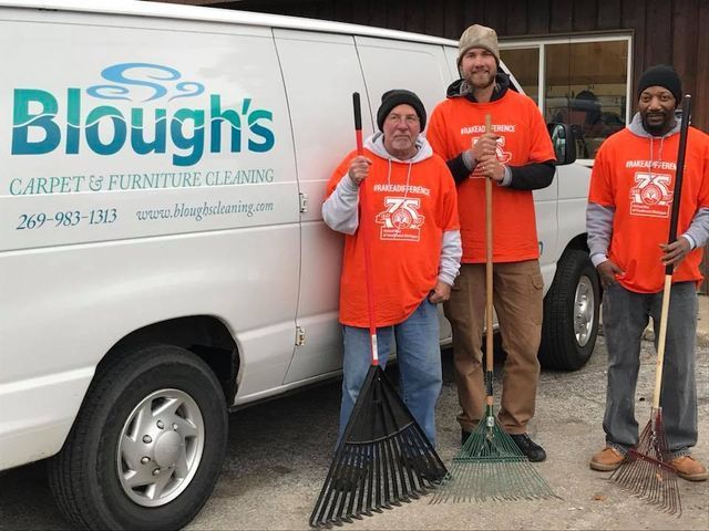 A group of men standing in front of a blough 's carpet and furniture cleaning van