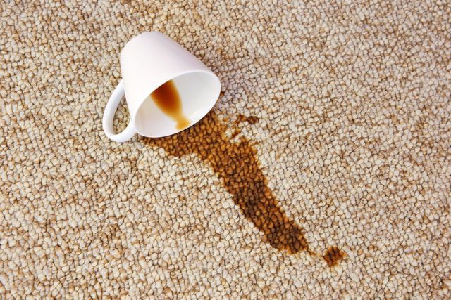 Spilled cup of coffee creating a stain on a light-colored carpet.