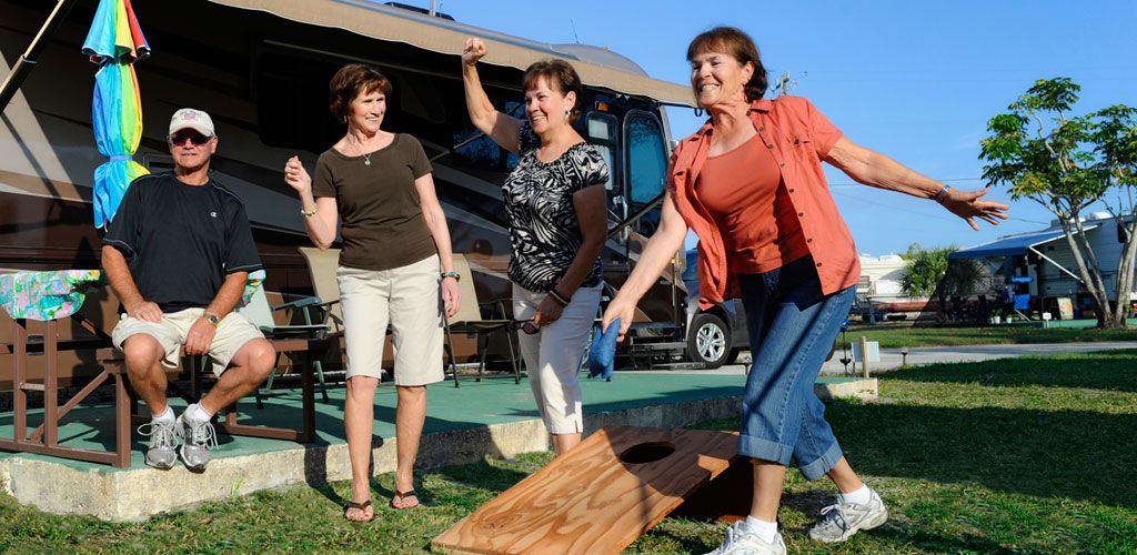 A group of people are playing a game of cornhole in front of a rv.