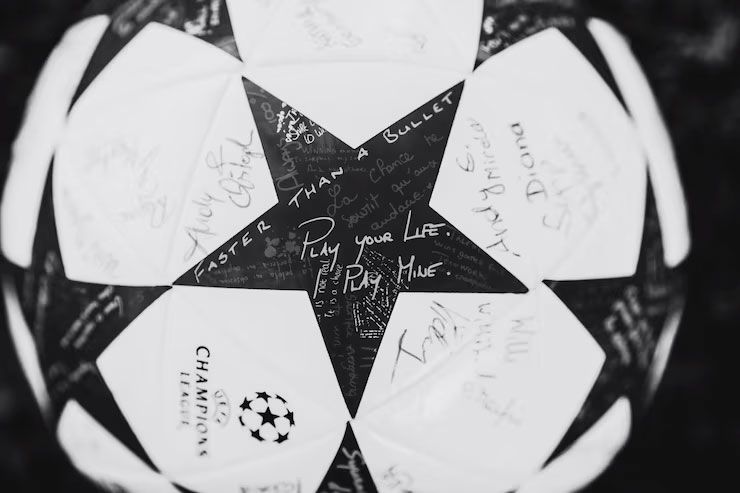 Black and white close-up of a UEFA Champions League soccer ball covered in various handwritten signatures and messages.
