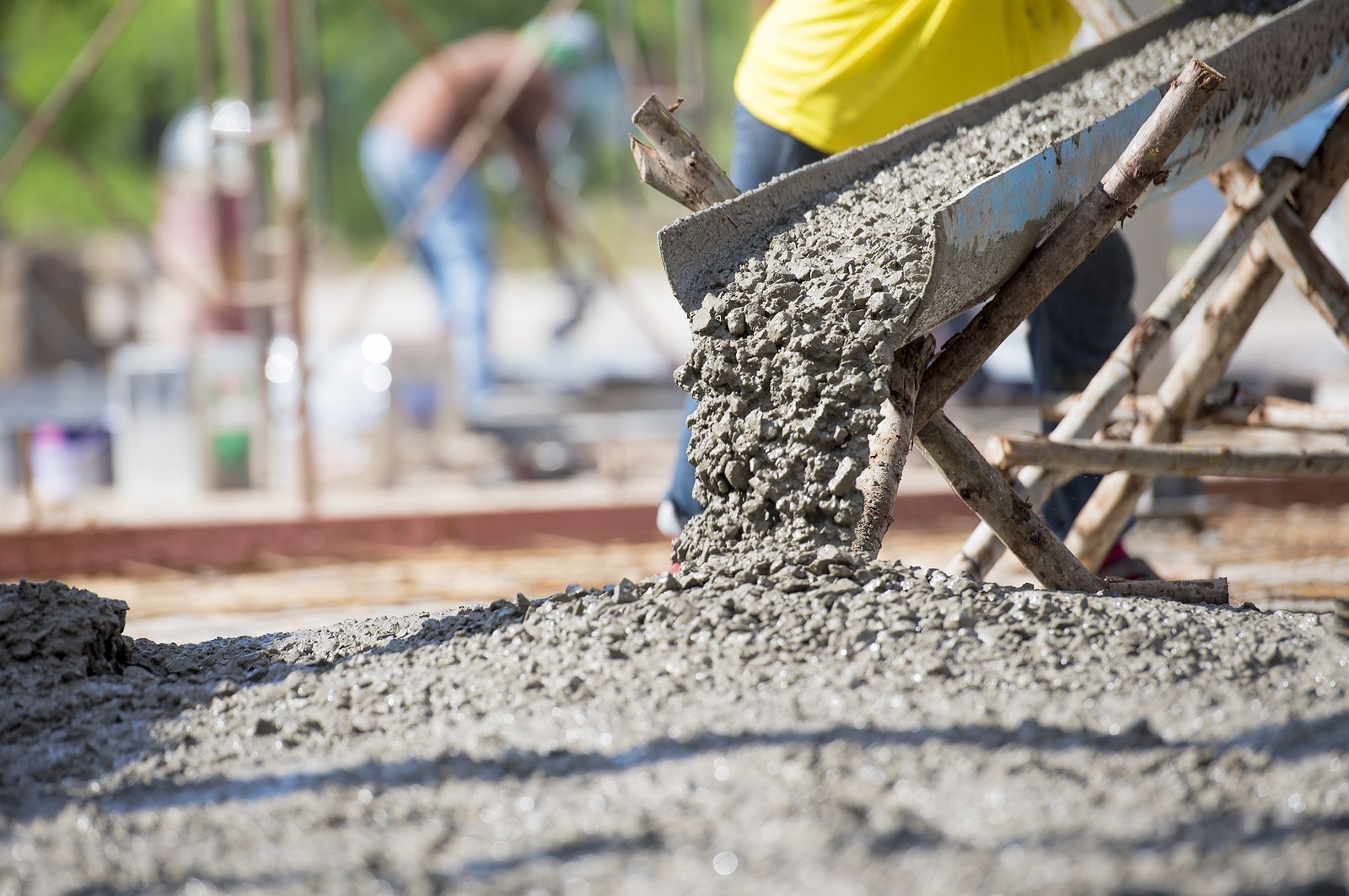 A man is pouring concrete into a wheelbarrow at a construction site.