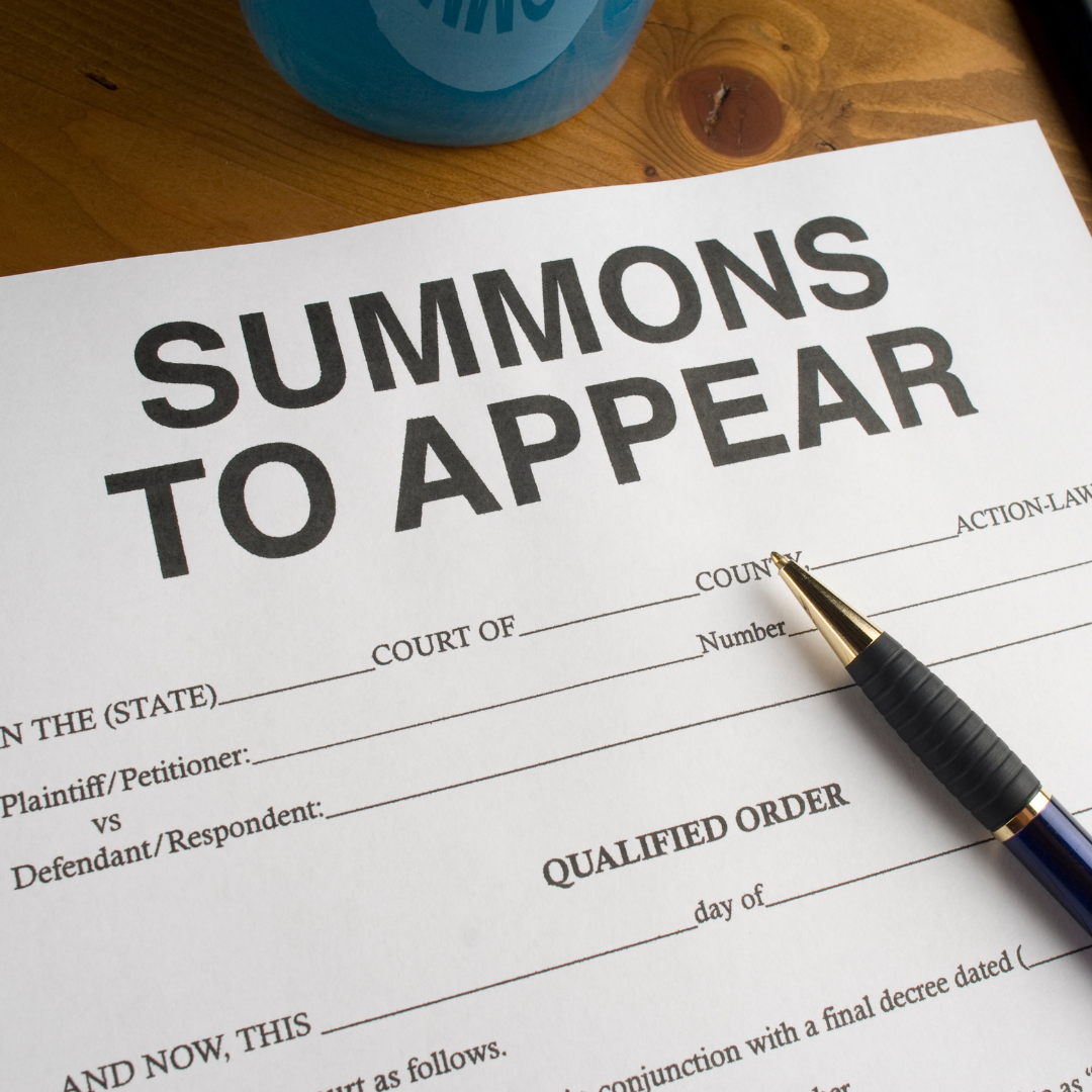 Summons to Appear document with a pen and a blue object on a wooden surface.