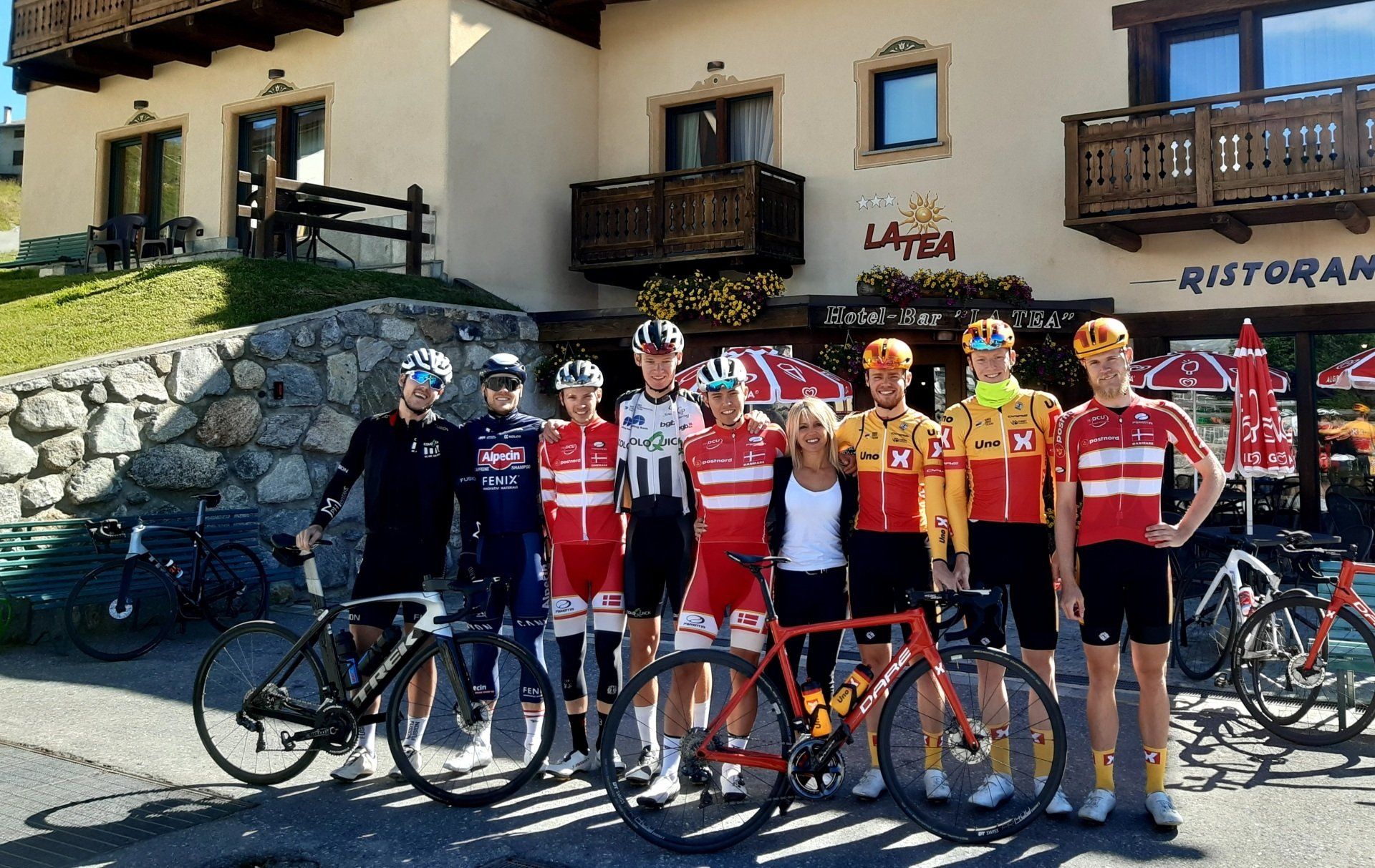 Gruppo di ciclisti in maglia in posa con le biciclette fuori da un ristorante.