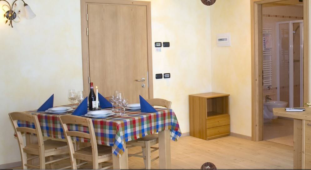 Sala da pranzo con tavolo apparecchiato per quattro persone, sedie in legno, tovaglia a quadri, porta per il bagno.