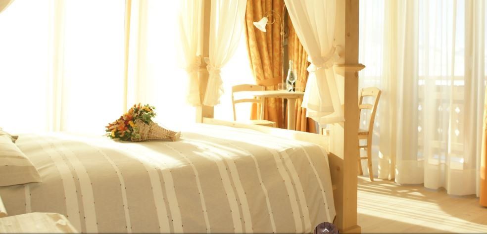 Camera da letto con letto a baldacchino, bouquet e luce solare che filtra attraverso tende trasparenti.