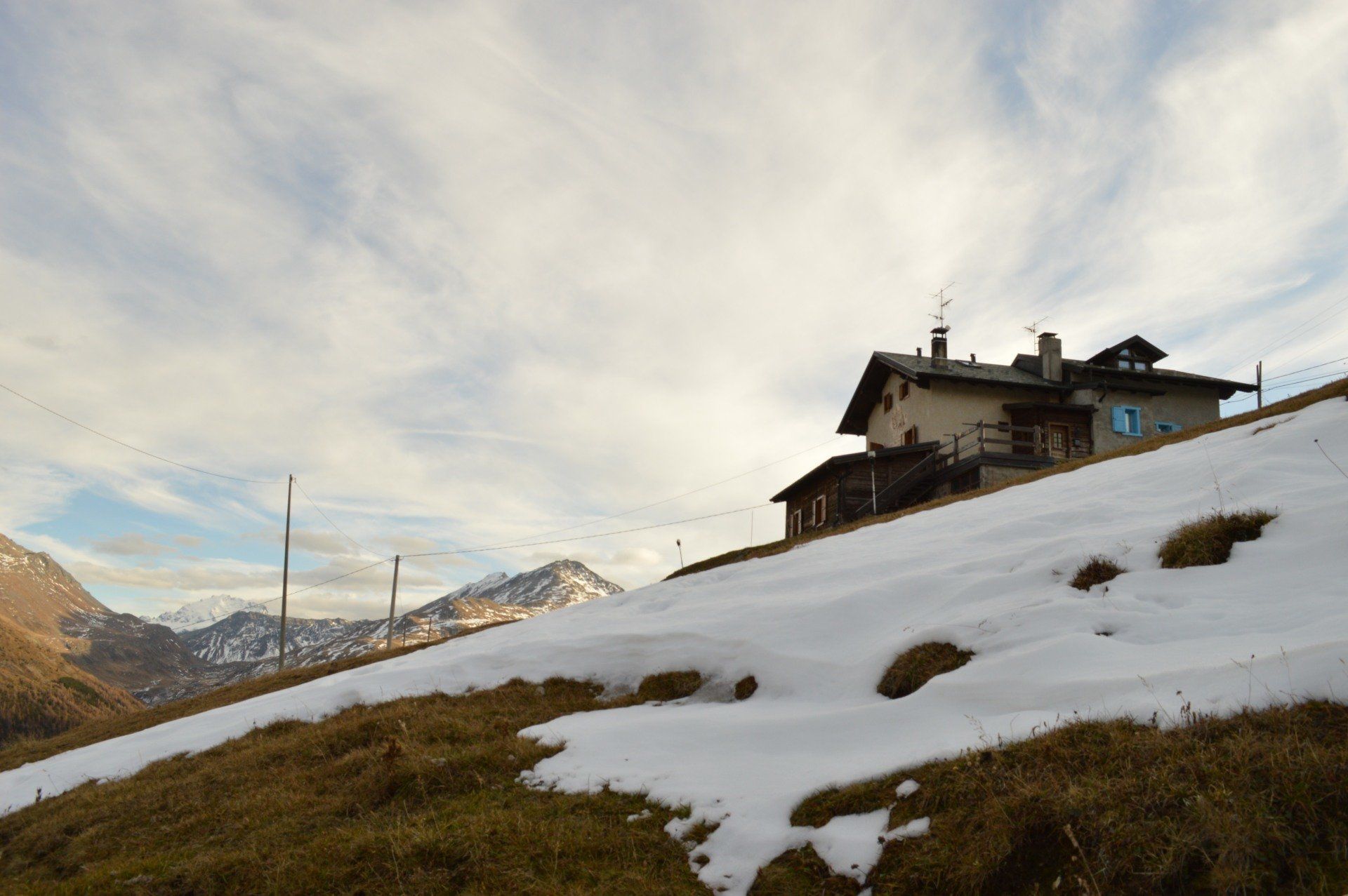 Pendio innevato con una casa in cima. Montagne sullo sfondo sotto un cielo nuvoloso.