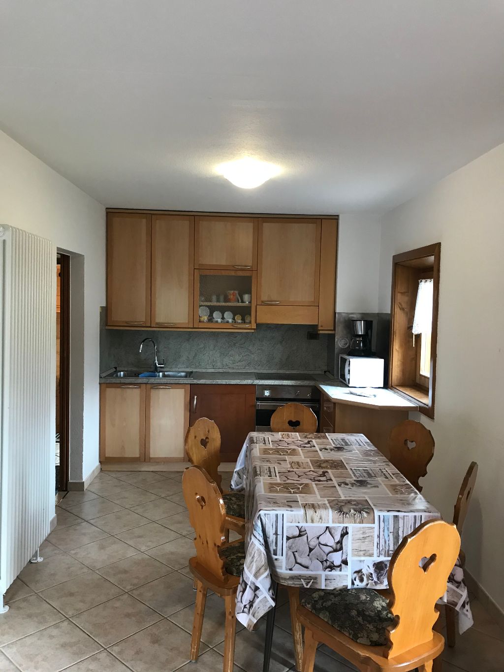 Cucina con mobili in legno, tavolo da pranzo con sedie e finestra.