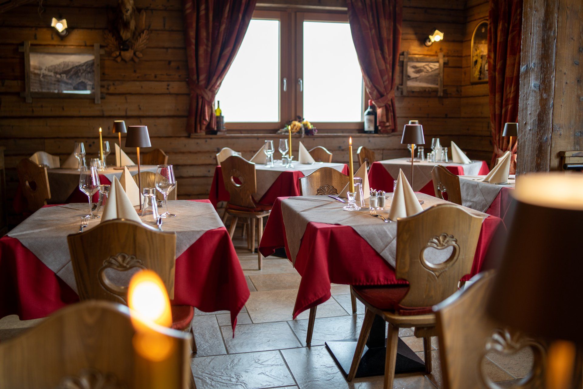 Interno del ristorante con pareti in legno, tovaglie rosse e sedie decorate.