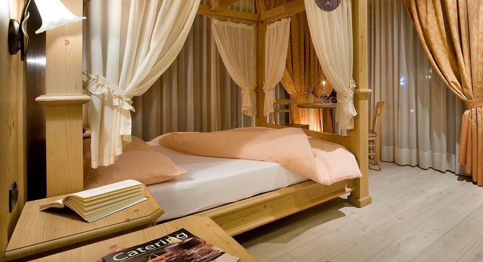 Accogliente camera da letto con letto a baldacchino, drappeggiato in tessuto color pesca, e comodino in legno con libri.