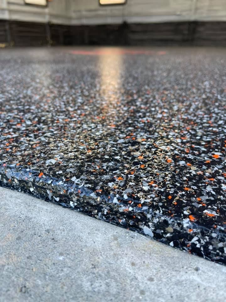 Close-up of a garage floor coated in a glossy epoxy finish with flecks of black, white, orange, and gray, next to a concrete edge.