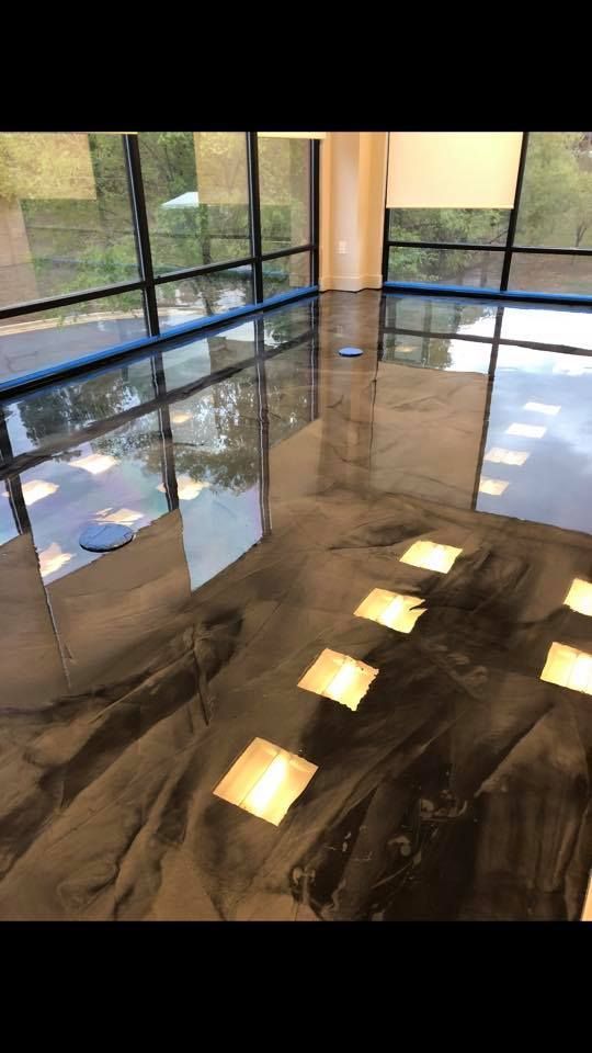 Shiny, metallic-looking epoxy floor reflecting a bright room with large windows. Blue tape lines the edges.
