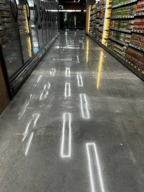 Polished concrete floor in a grocery store aisle with rectangular inset lighting reflecting the overhead lights.