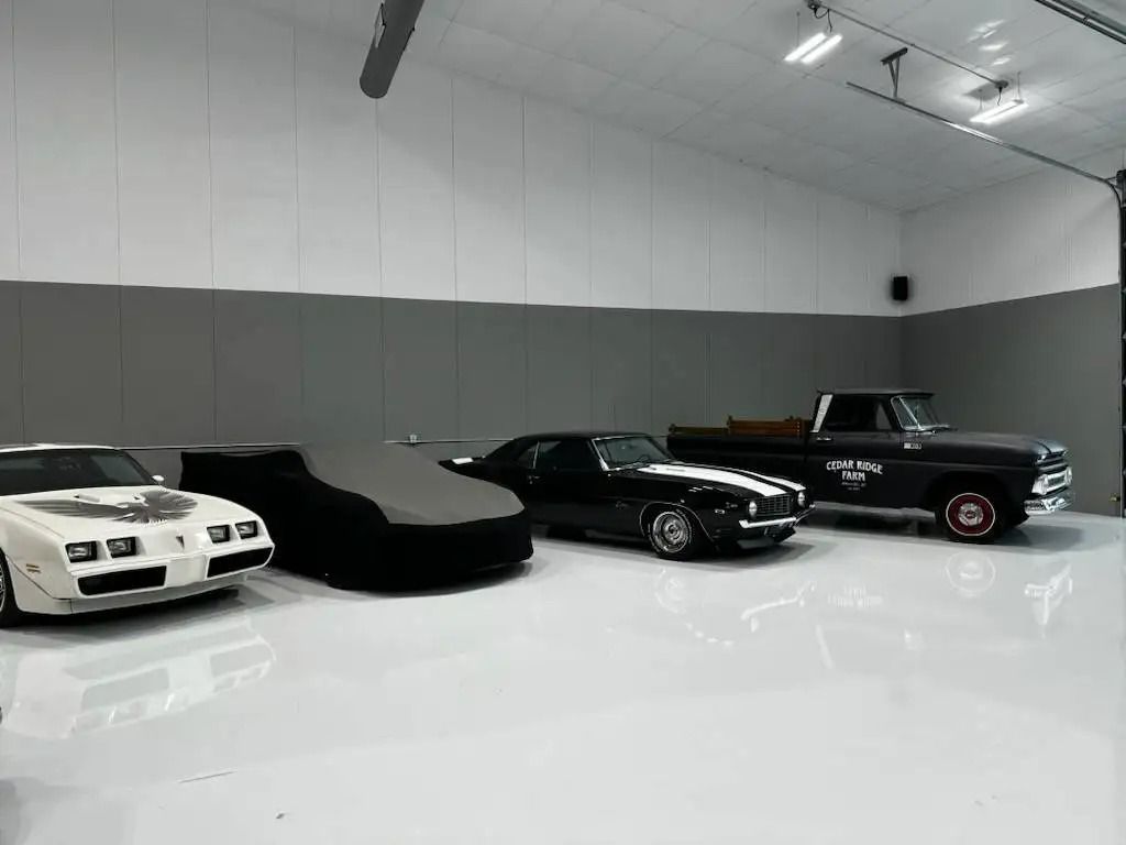 Four classic cars are parked in a spacious, modern garage with a bright, white floor and gray walls.