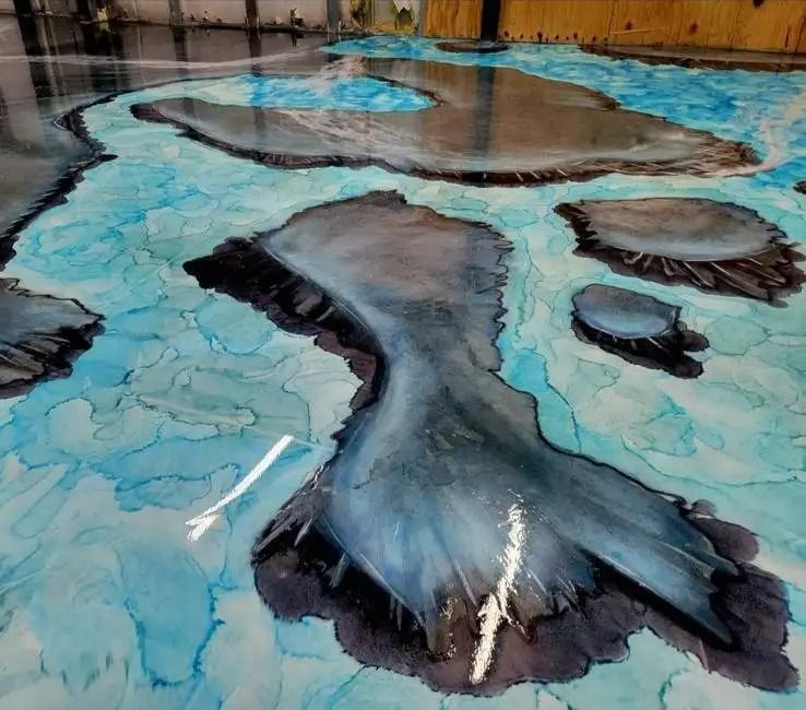 Epoxy resin floor art depicts islands in shades of gray and blue. The flowing resin creates a unique, water-like effect.