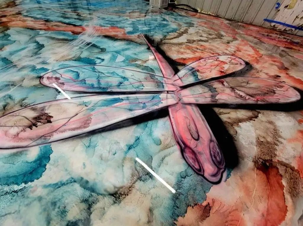Dragonfly artwork on a colorful epoxy floor with blues, reds, and browns. The dragonfly has a pink, red, and white pattern.