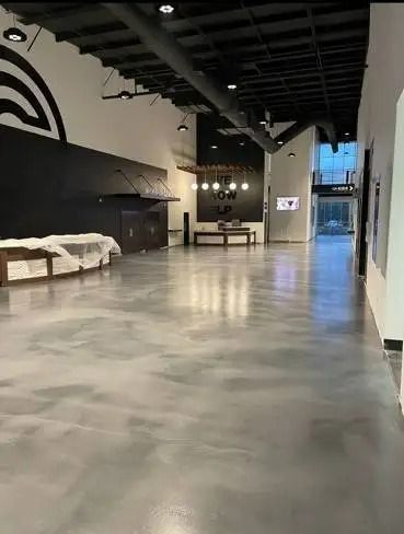 Spacious, modern venue with polished gray floors, black accent walls, and a chandelier. The space appears empty.