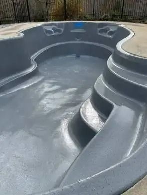 Empty gray swimming pool with curved edges and steps. Concrete surrounds the pool.
