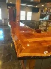A polished wooden bar in a commercial setting, with a shiny, amber-colored surface and a rough, natural edge.