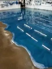 Blue epoxy floor resembling a beach scene, with a brown floor area and white cylinders embedded in the blue “water.”