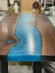 A wooden table with a blue epoxy resin river down the center, set in a workshop.