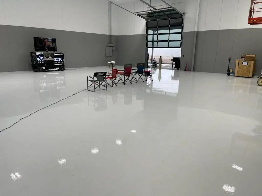 Spacious, white-floored room with an open garage door. Several chairs are arranged in the center; equipment and a gaming setup are in the background.