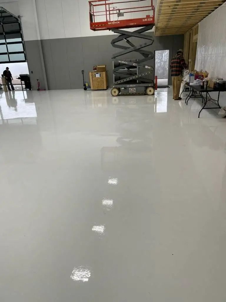 A wide, light-colored, polished floor reflects the interior of a large, open space. A scissor lift and boxes are visible in the background.