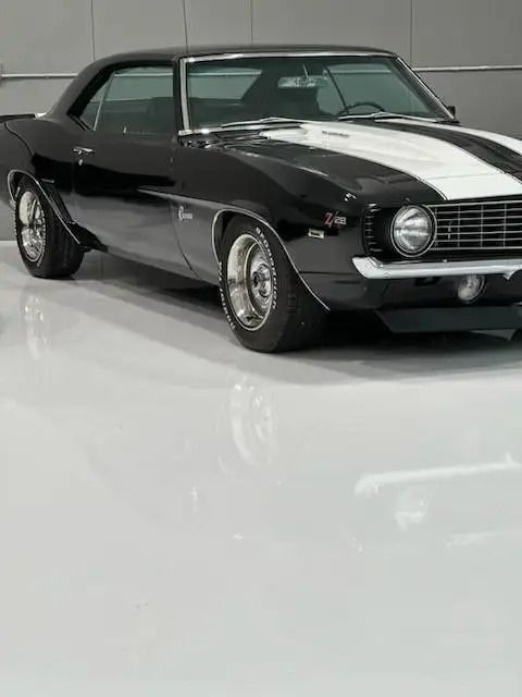 Black and white 1969 Chevrolet Camaro muscle car with racing stripes, parked on a glossy white floor in a showroom.