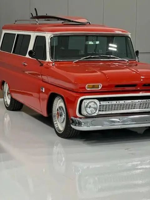 Red and white vintage Chevrolet Suburban with chrome details and a roof rack, parked in a bright studio.