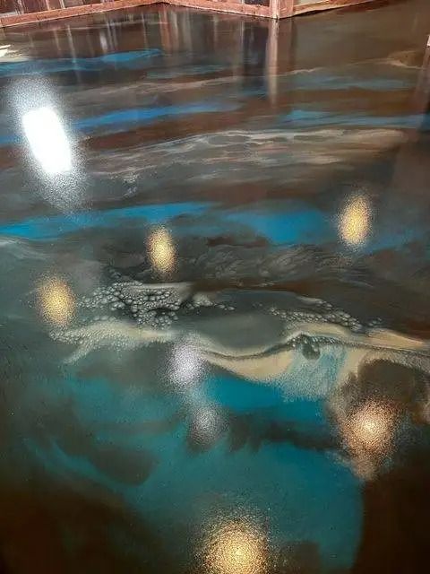 Metallic epoxy floor with blue, brown, and silver swirls reflecting light. Surface imperfections visible.