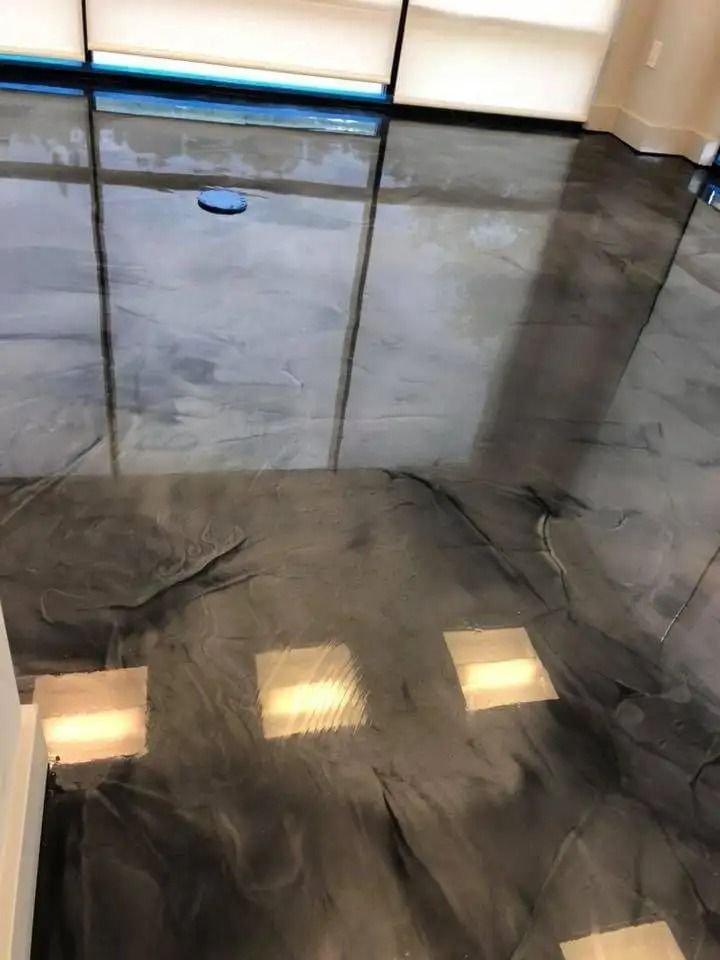 Shiny, dark gray epoxy flooring with a metallic sheen, reflecting light from large windows and built-in lights.