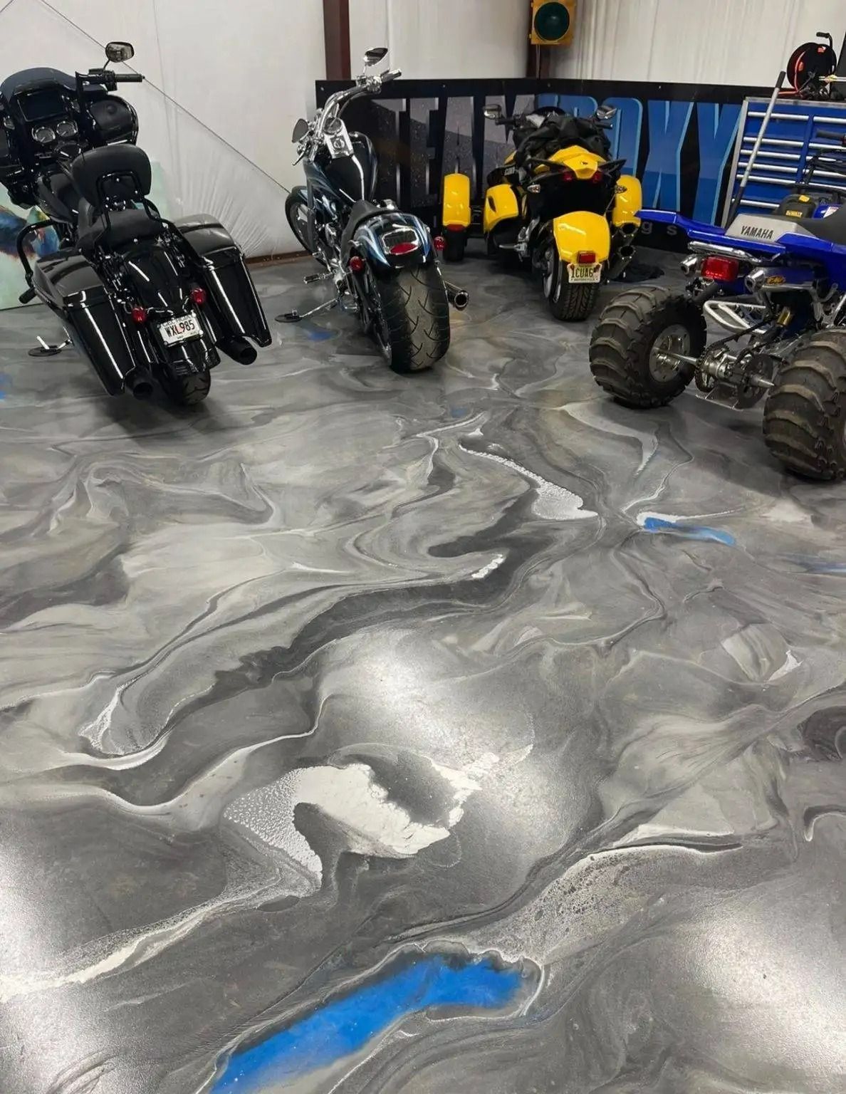 Motorcycles and an ATV on a decorative gray, blue, and white epoxy floor inside a garage.