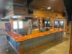 An empty wooden bar with a textured countertop, mounted beneath wooden beams. The bar is surrounded by grey corrugated metal.