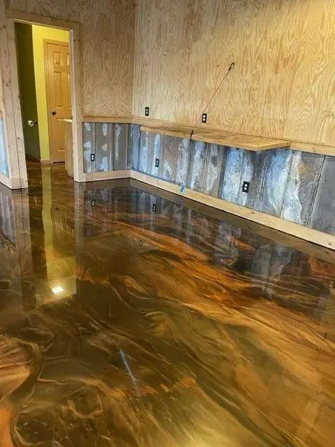 Shiny gold and brown epoxy floor in a room with unfinished plywood walls and a low concrete ledge.