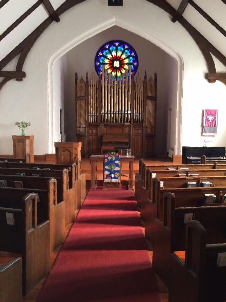Sanctuary of the church with pews, the chalice table, pew, and organ. aisle down the middle of the image.