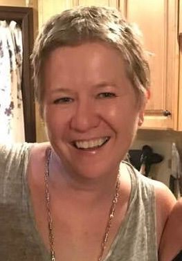 a white middle aged woman with short grayish blonde hair smiling at the camera