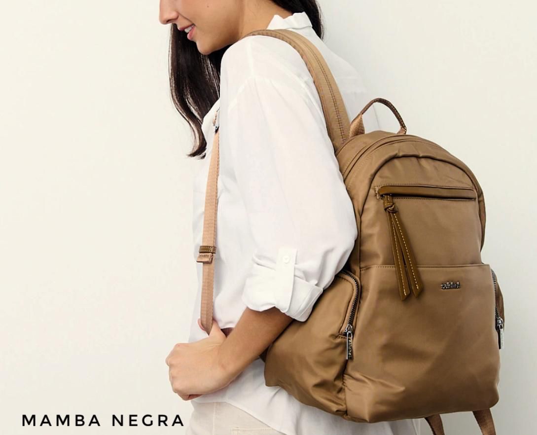 Una mochila de nailon minimalista de color bronce con múltiples bolsillos con cremallera, apoyada contra una pared blanca.