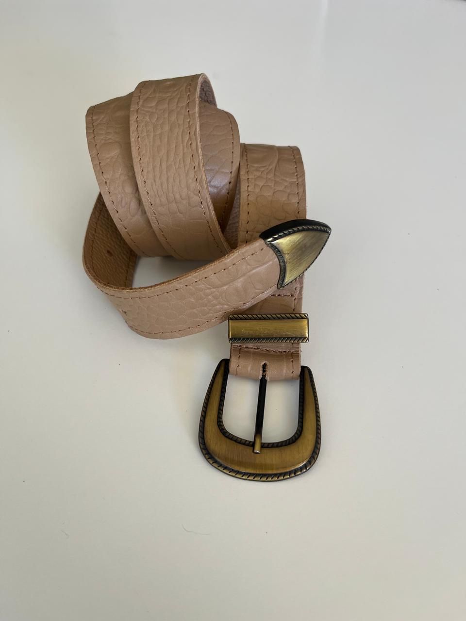 Un cinturón texturizado de color bronce enrollado sobre una superficie blanca,
