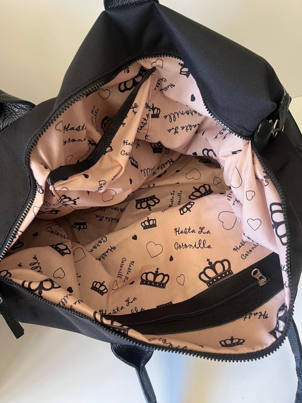 Bolso de lona negro texturizado con dos asas superiores y una correa de hombro ancha con la marca 