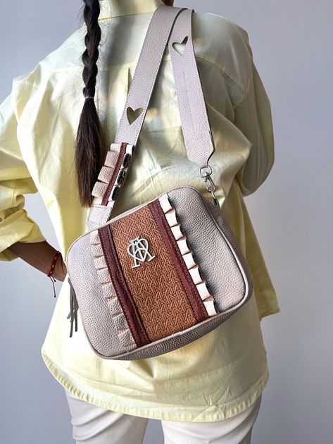 Una persona lleva un vestido largo marrón con flores y sostiene frente a ella un bolso de hombro grande, 