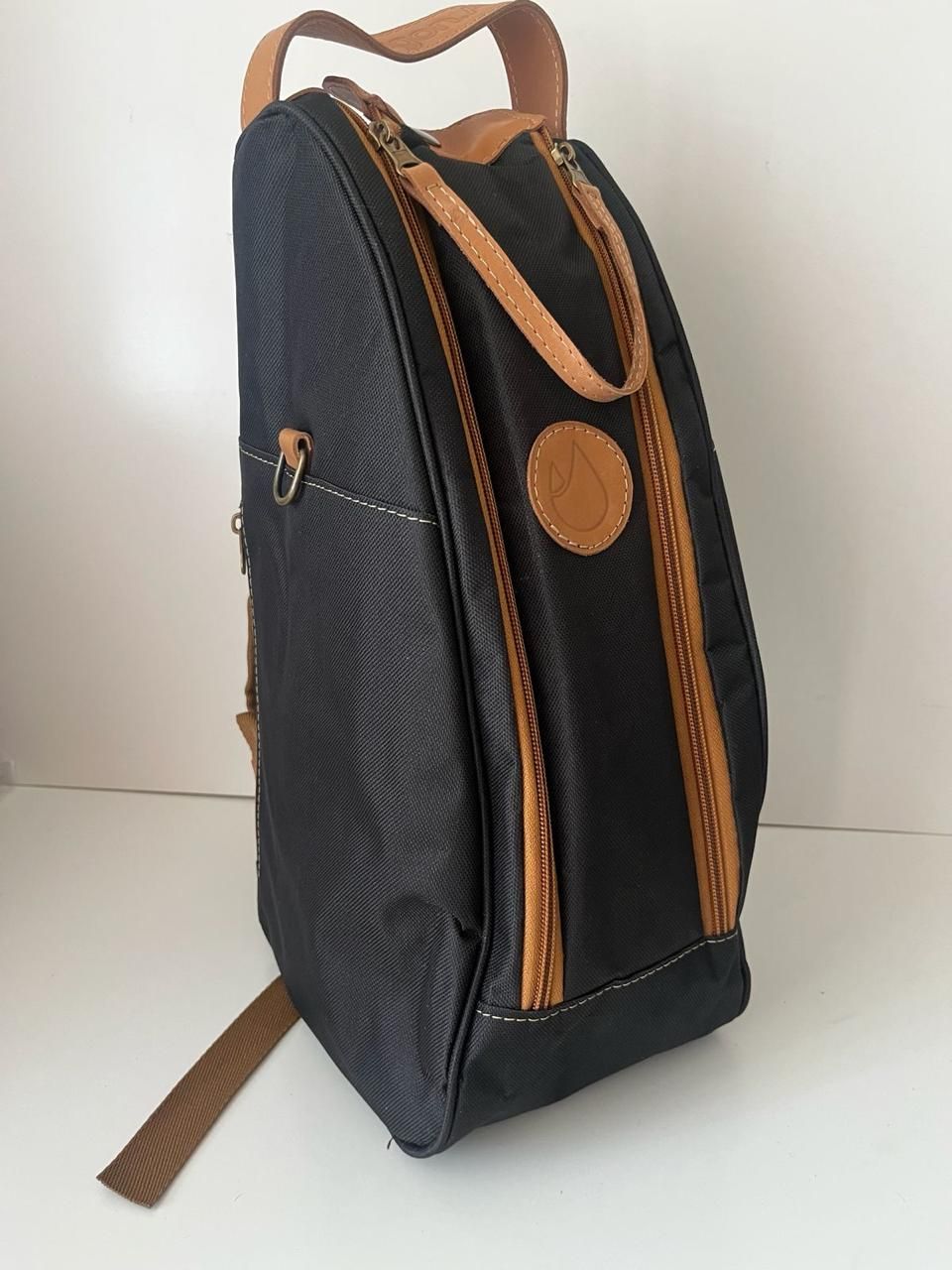 Una mochila negra con detalles de cuero color canela y una taza de marca a juego junto a ella sobre un fondo blanco.