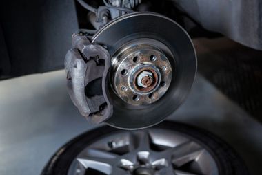 A car's brake disc and caliper assembly with the wheel removed, shown in a garage or workshop setting.